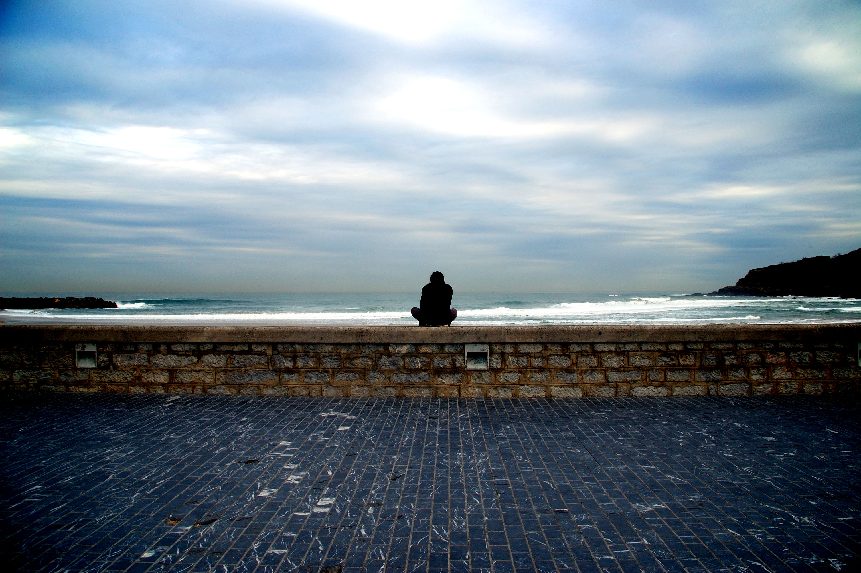 una persona solitaria viendo con nostalgia un atardecer mirando al mar