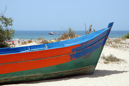 una patera de color naranja azul y verde abandonada en la playa al fondo se ve el mar