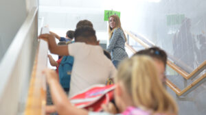 Niños de Primaria se dirigen a su aula bajo la mirada de una trabajadora del centro escolar.